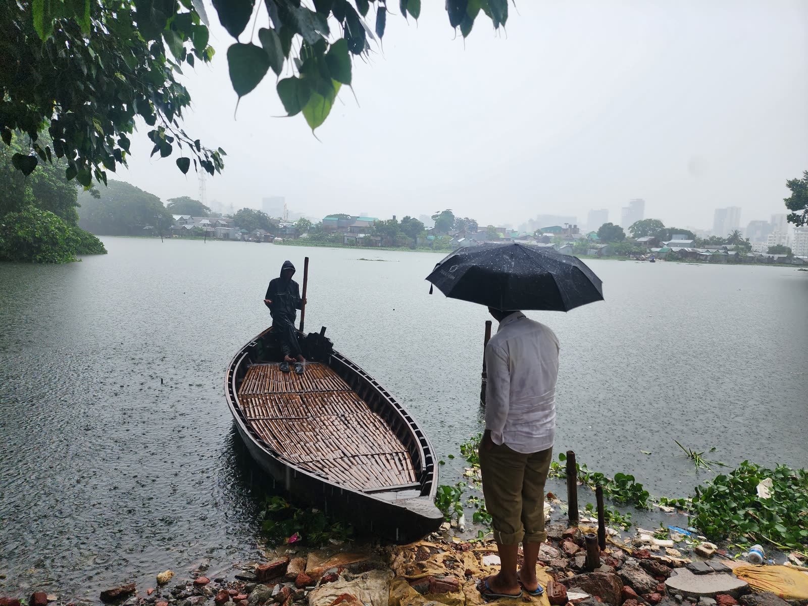 People waiting to board a small boat at a river crossing in the rain in Bangladesh